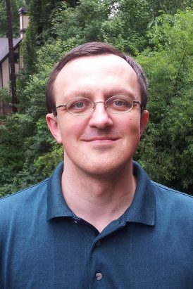 Smiling headshot, wearing glasses and a collared shirt