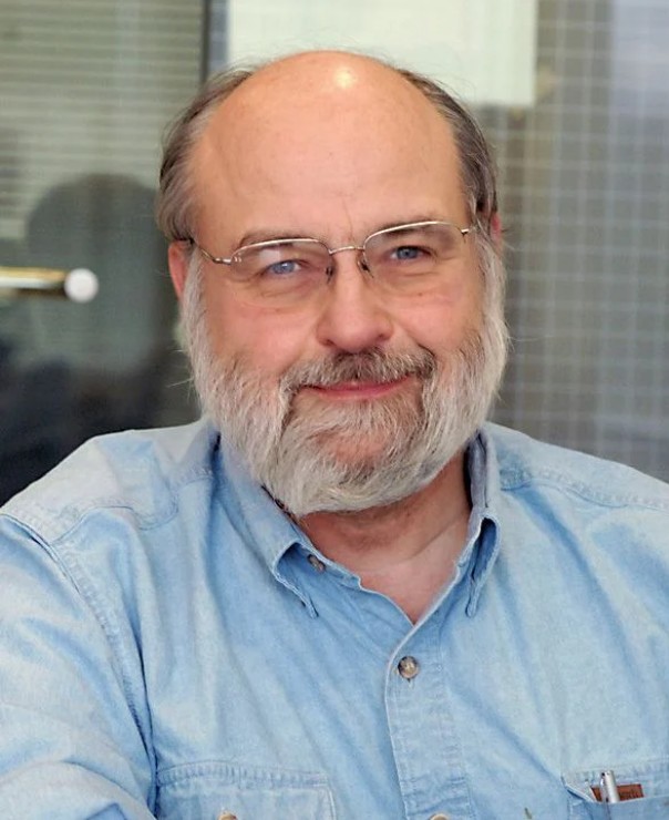 Headshot, wearing glasses, a beard and blue collared shirt.