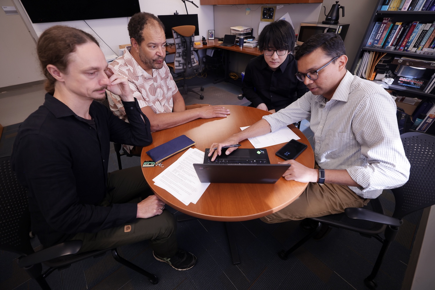 The main players of the theory team, Florian and Kira (from the left), discuss results with the lead experimenters, Jiang and Deotare (continuing from the left). Their team has demonstrated the first directed, gated flow of chargeless quantum information carriers called excitons at room temperature. Photo: Brenda Ahearn/Michigan Engineering