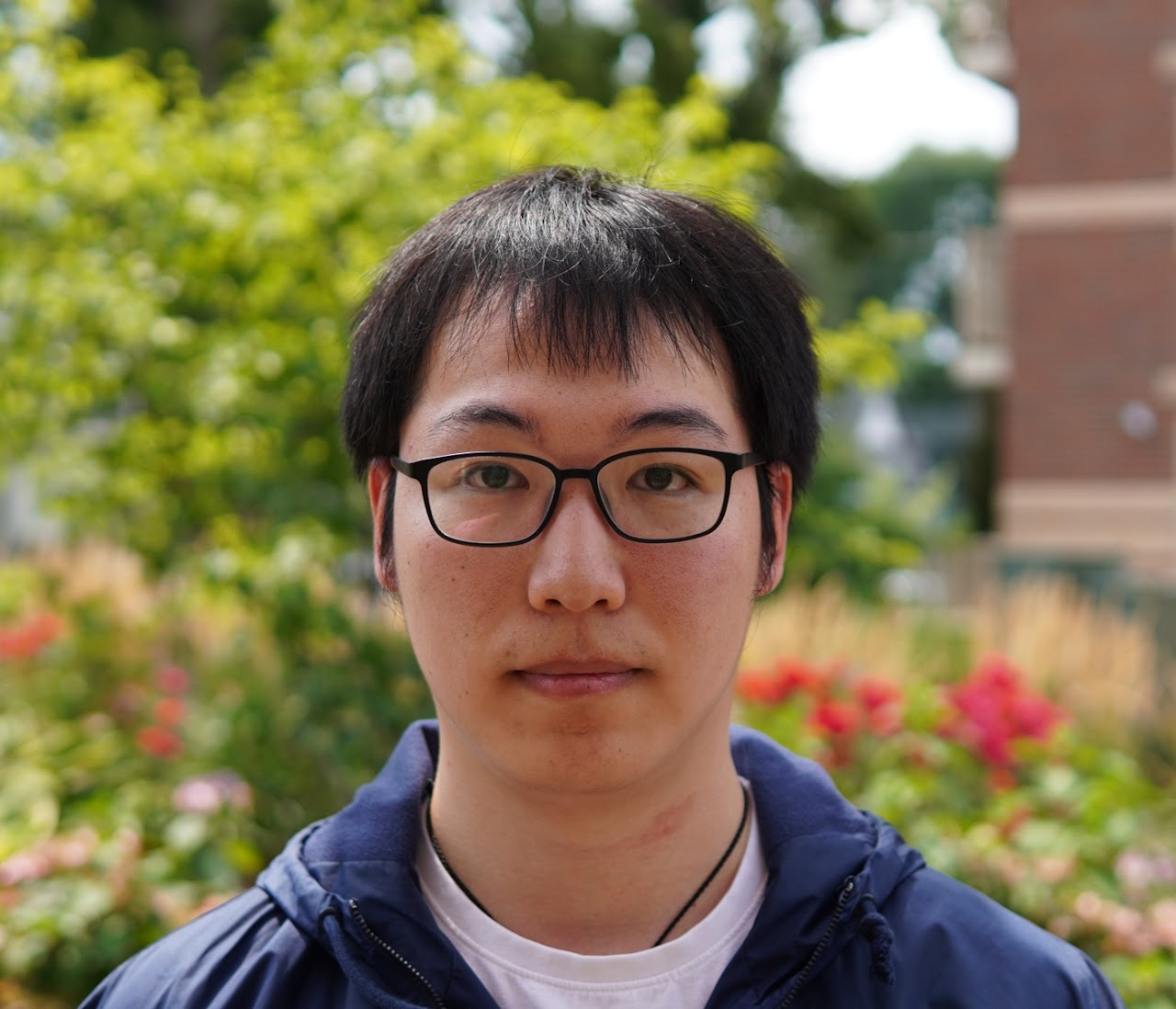 A headshot outside, in front of a tree, wearing glasses and a sweatshirt.